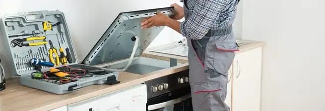 Cooktop repair technician lifting a built-in stovetop for service in Chandler, AZ