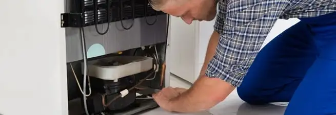 Refrigerator repair technician servicing the compressor and condenser area in Chandler, AZ