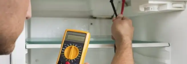 Refrigerator repair technician testing electrical components with a multimeter in Chandler, AZ