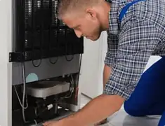 Refrigerator repair technician servicing the compressor and condenser area in Chandler, AZ